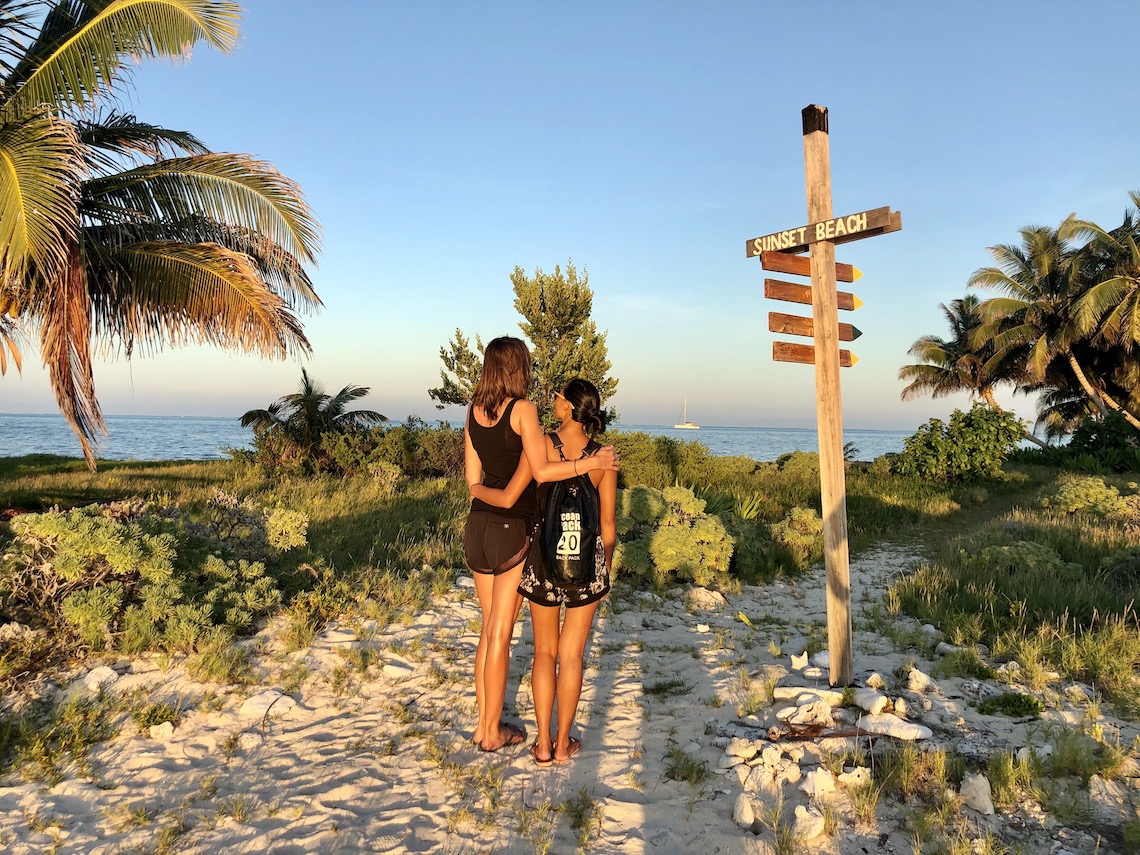Two women in front of a signpost in Lighthouse Reef at sunset