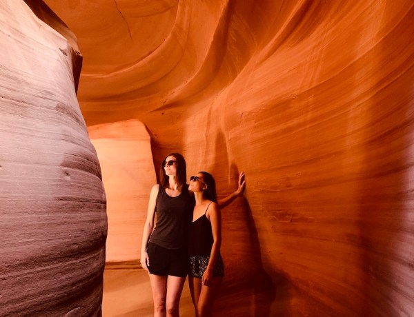 Two woman standing inside Upper Antelope Canyon, surrounded by red sand stone walls