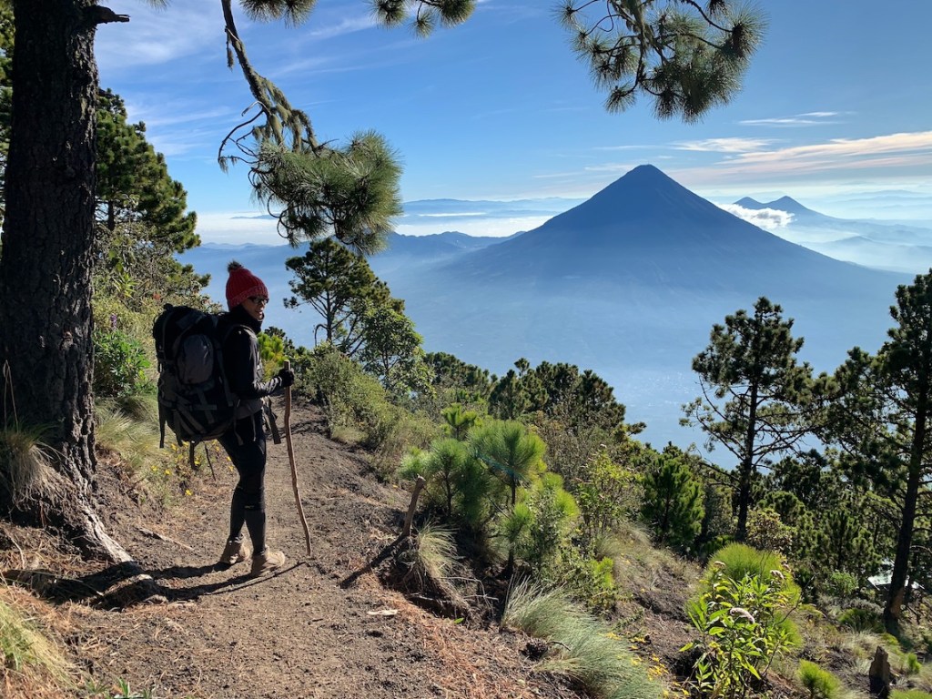 Woman hiking along Acatenango base camp on a clear day overlooking surrounding volcanoes in Guatemala 